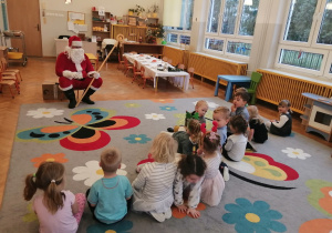 Dzieci siedzą na dywanie słuchając co mówi Mikołaj